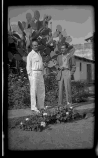 Witter Bynner (left) with Robert Hunt, on sidewalk near cactus and  geraniums